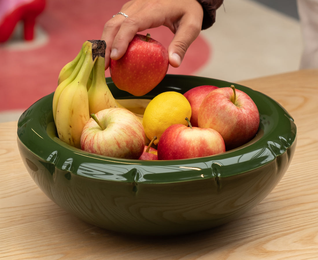 A glossy dark green ceramic Blow Up bowl with a flared rim and subtle embossed details filled with fruit.