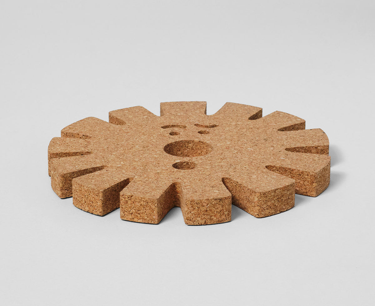 Sun Face Medium Cork Trivet by Wrap lying flat on a white surface.