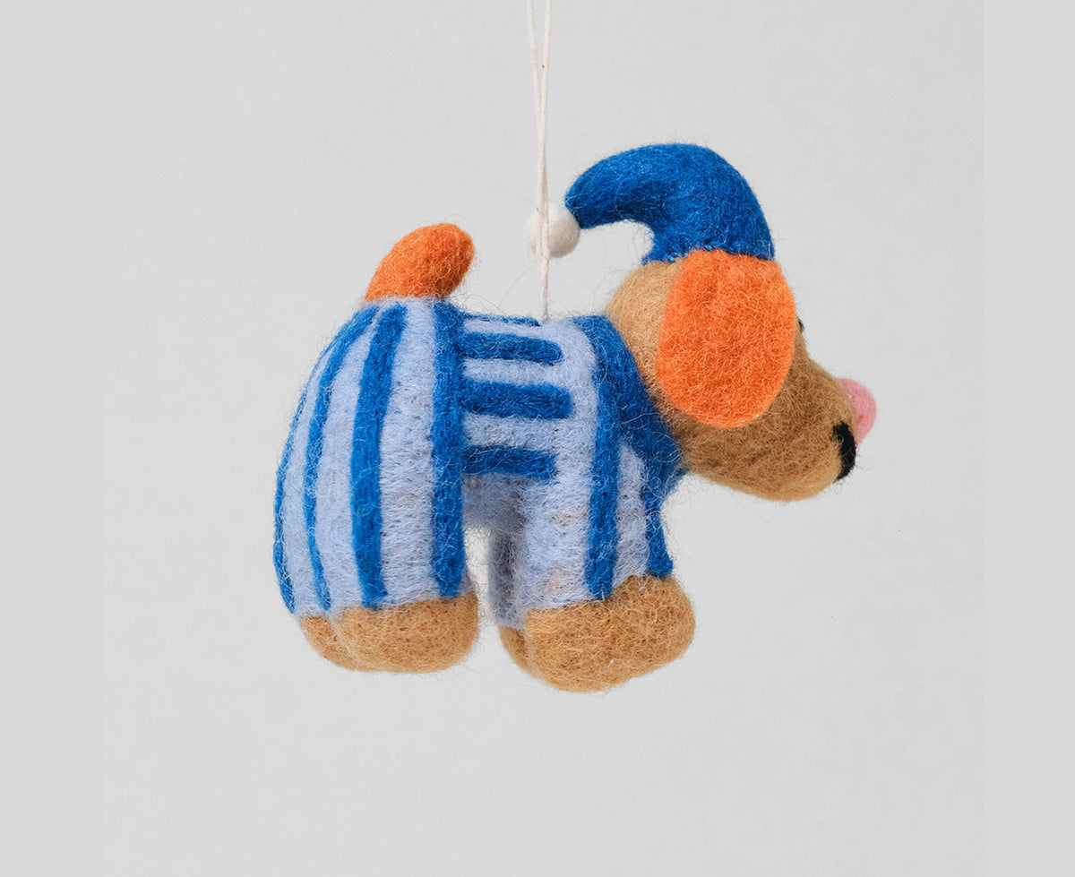 A felt dog Christmas ornament wearing a blue pointed hat and a blue-and-white striped sweater, with orange floppy ears and a pink nose seen from the side.