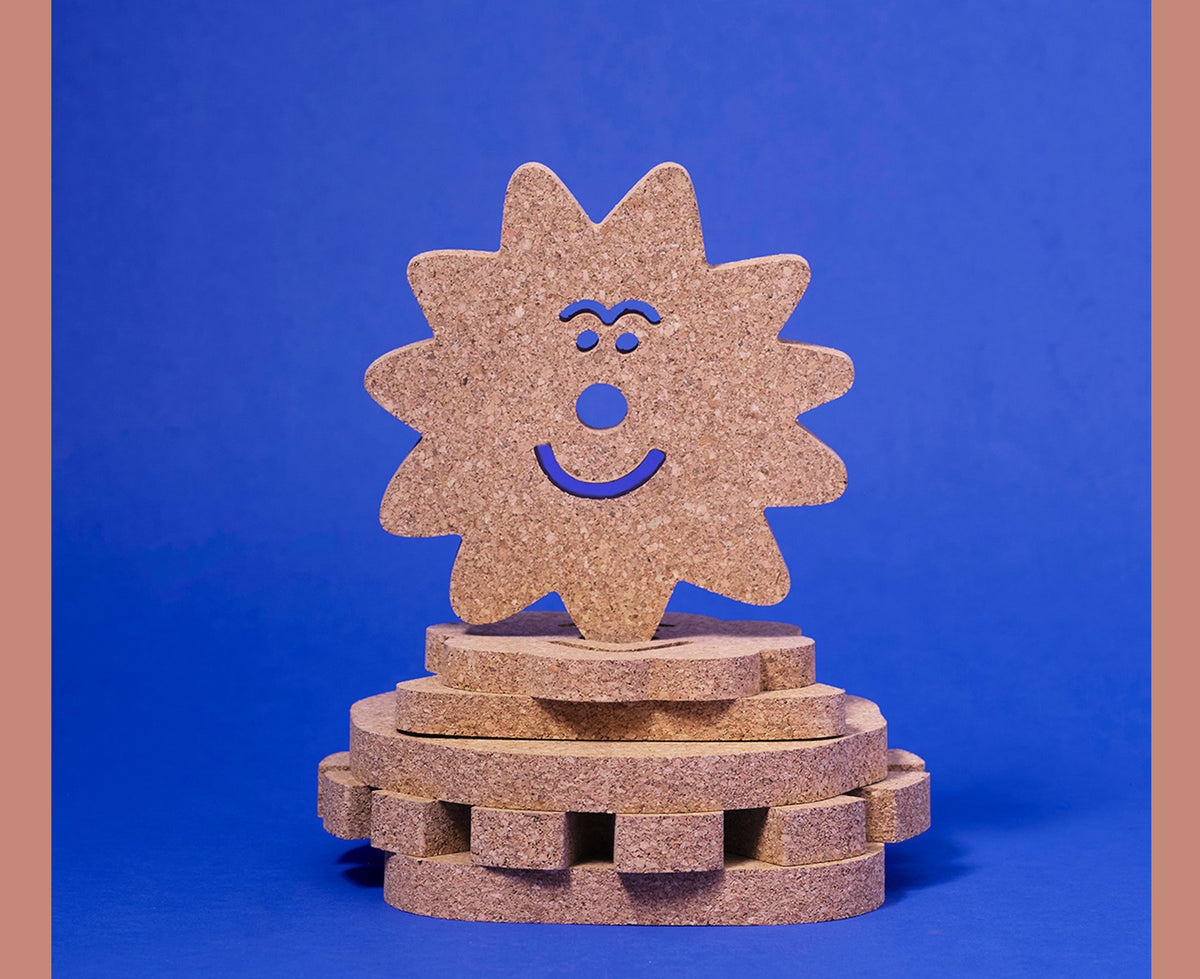 A stack of cork trivets by Wrap shaped like smiling sun, star and flower, on a bright blue background.