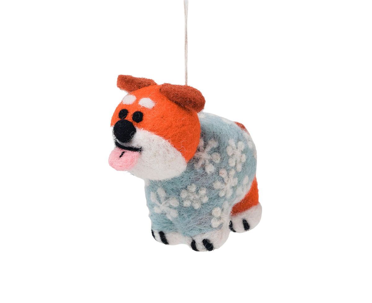 A felt dog ornament wearing a light blue and white floral sweater, hanging from a thin white string against a solid white background.