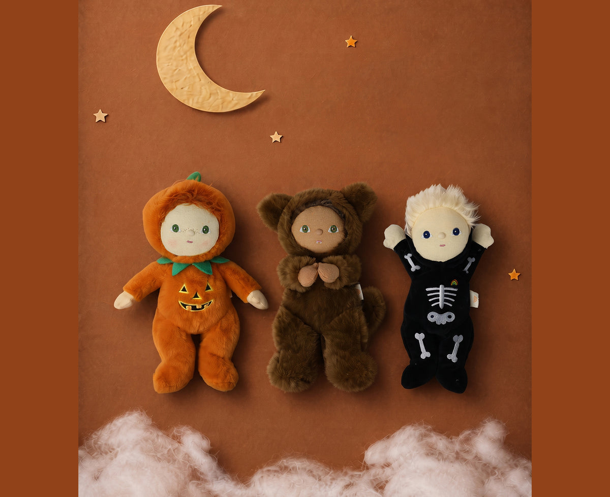 A plush werewolf cozy dinkum doll wearing a brown hooded outfit with floppy ears with two other dolls on an orange background.