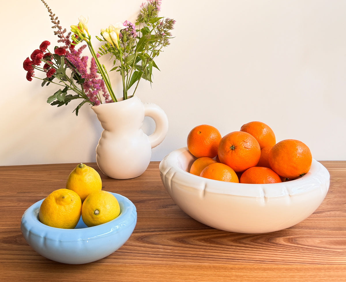 Three ceramic Blow Up items in light blue, white, and off-white on a wooden table.