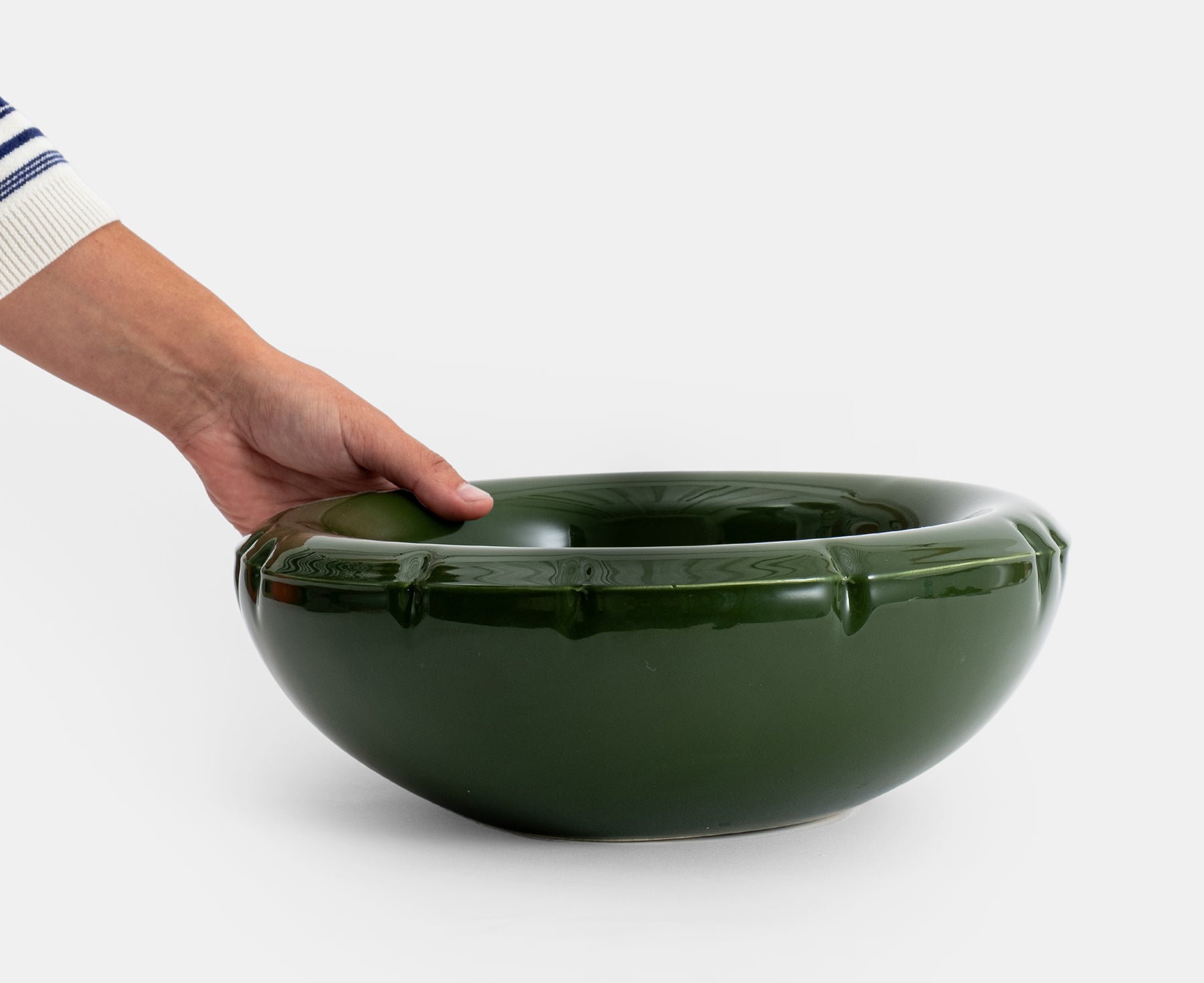 A glossy dark green ceramic Blow Up bowl with a flared rim and subtle embossed details and hand.