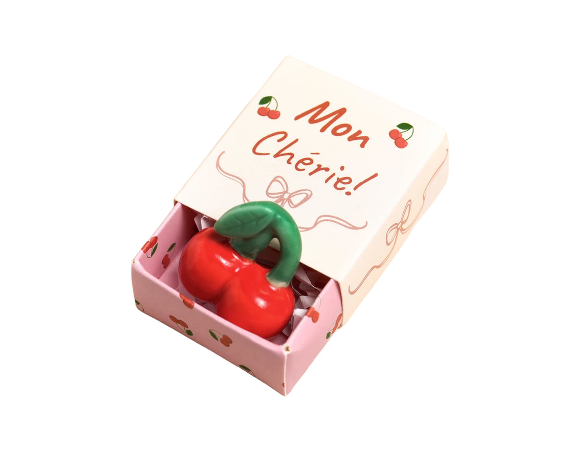 A cherry-shaped ceramic figurine displayed in a pink gift box with the French text &