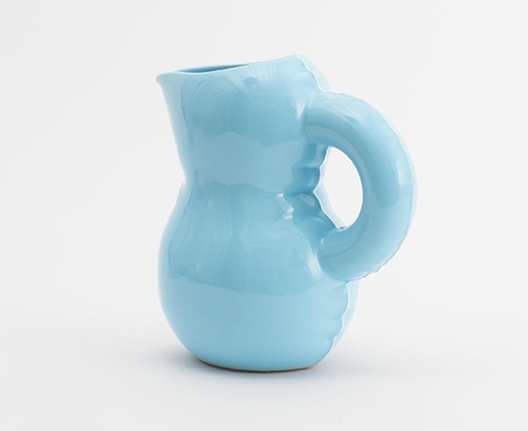 A light blue Blow Up ceramic pitcher by Home Studyo with a rounded, sculptural design, scalloped edges, and a curved handle.