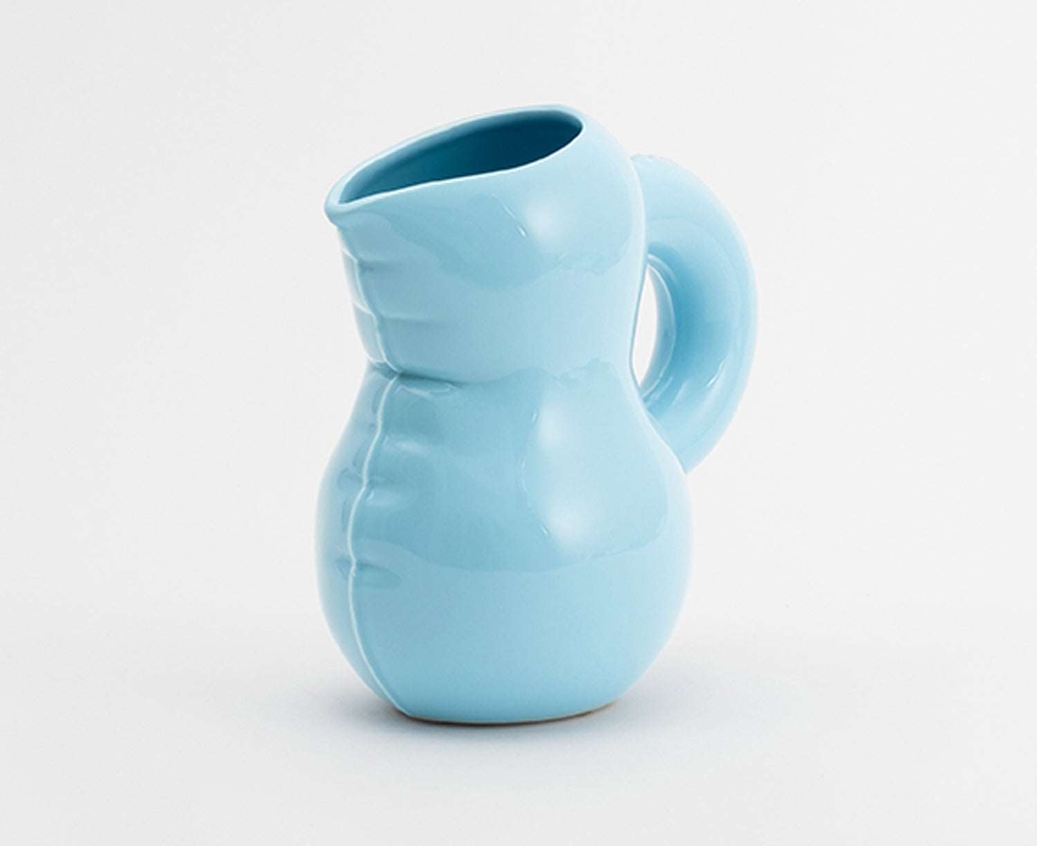 A light blue Blow Up ceramic pitcher by Home Studyo with a rounded, sculptural design, scalloped edges, and a curved handle.