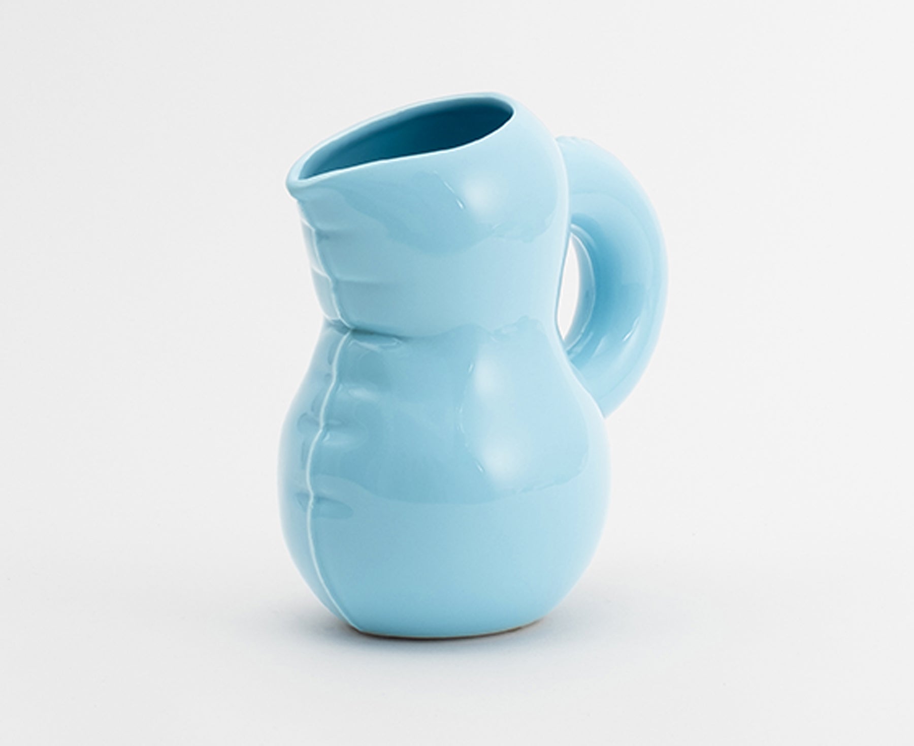 A light blue Blow Up ceramic pitcher by Home Studyo with a rounded, sculptural design, scalloped edges, and a curved handle.