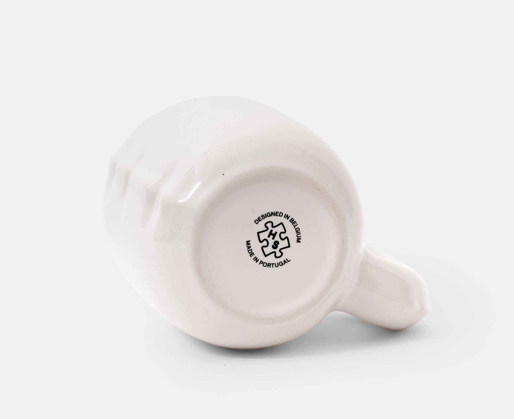 The bottom of a glossy white ceramic Gaston Blow Up Mug by Home Studyo with a sculpted, organic handle and side details.