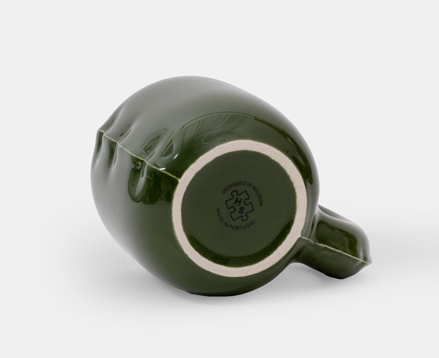 The bottom of a glossy dark green ceramic Gaston Blow Up Mug by Home Studyo with a sculpted, organic handle and side details.