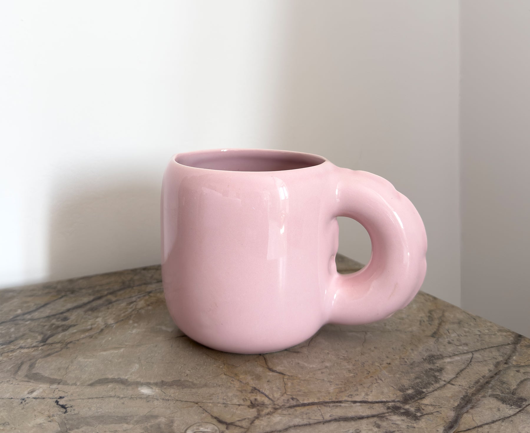 A glossy pink ceramic Gaston Blow Up Mug by Home Studyo with a sculpted, organic handle and side details on a table.