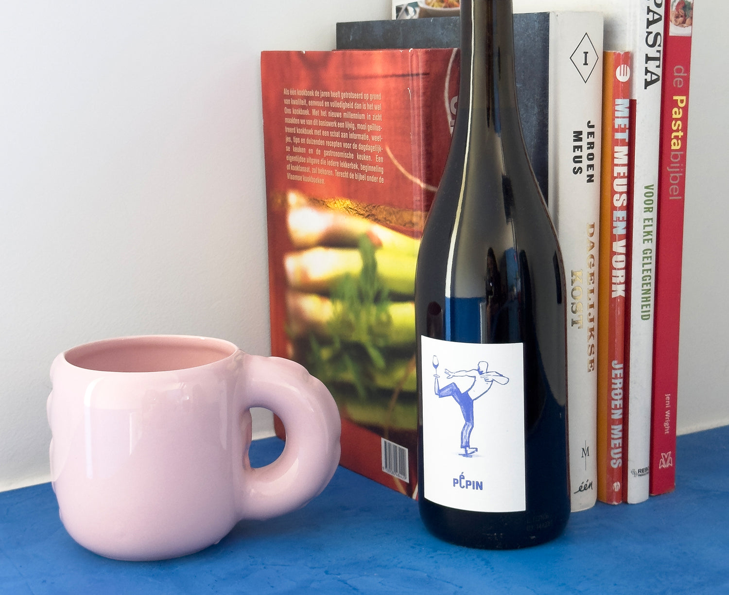 A glossy pink ceramic Gaston Blow Up Mug by Home Studyo with a sculpted, organic handle and side details with books and wine.