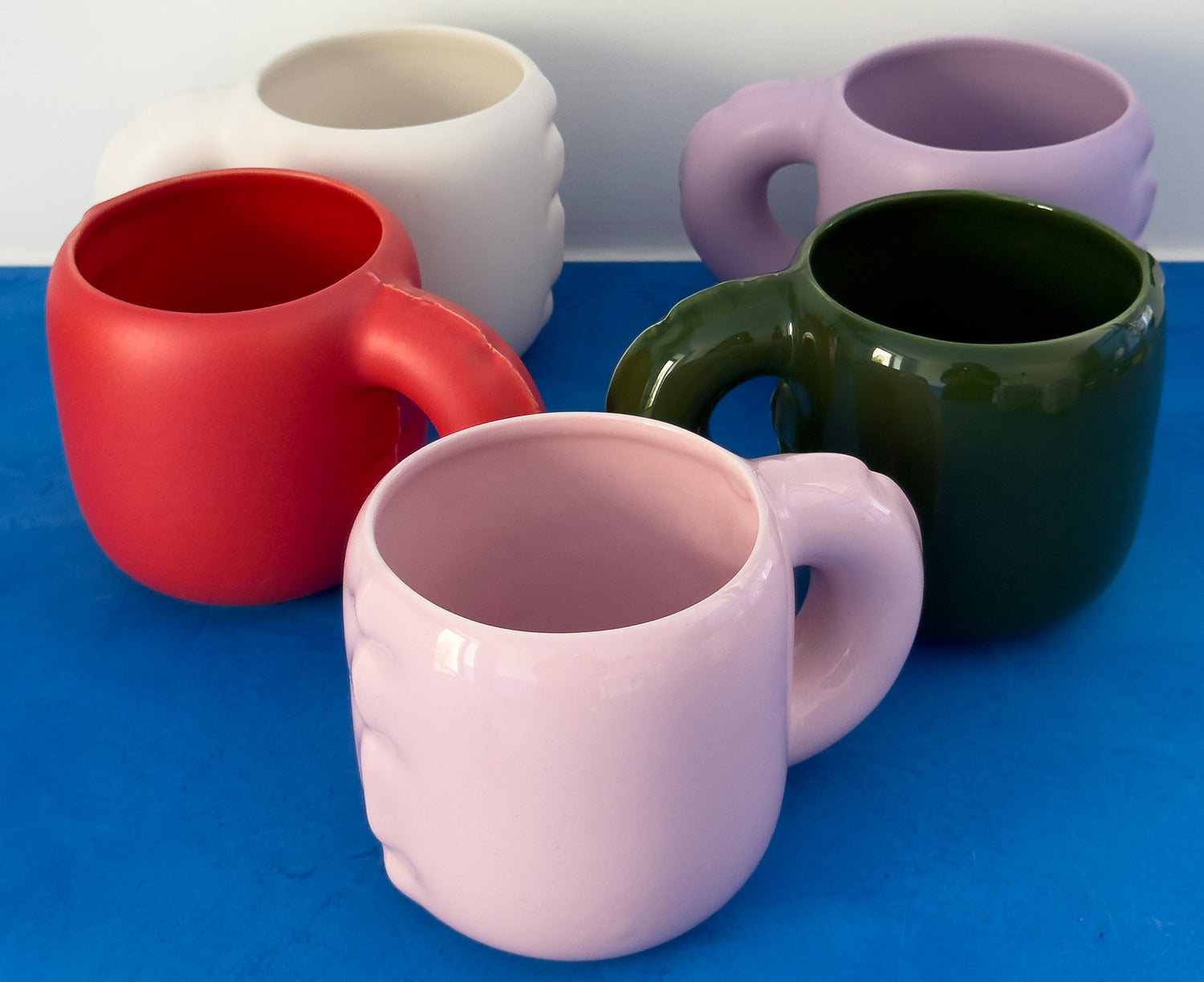 Glossy ceramic Gaston Blow Up Mugs by Home Studyo with sculpted, organic handles on a blue table.