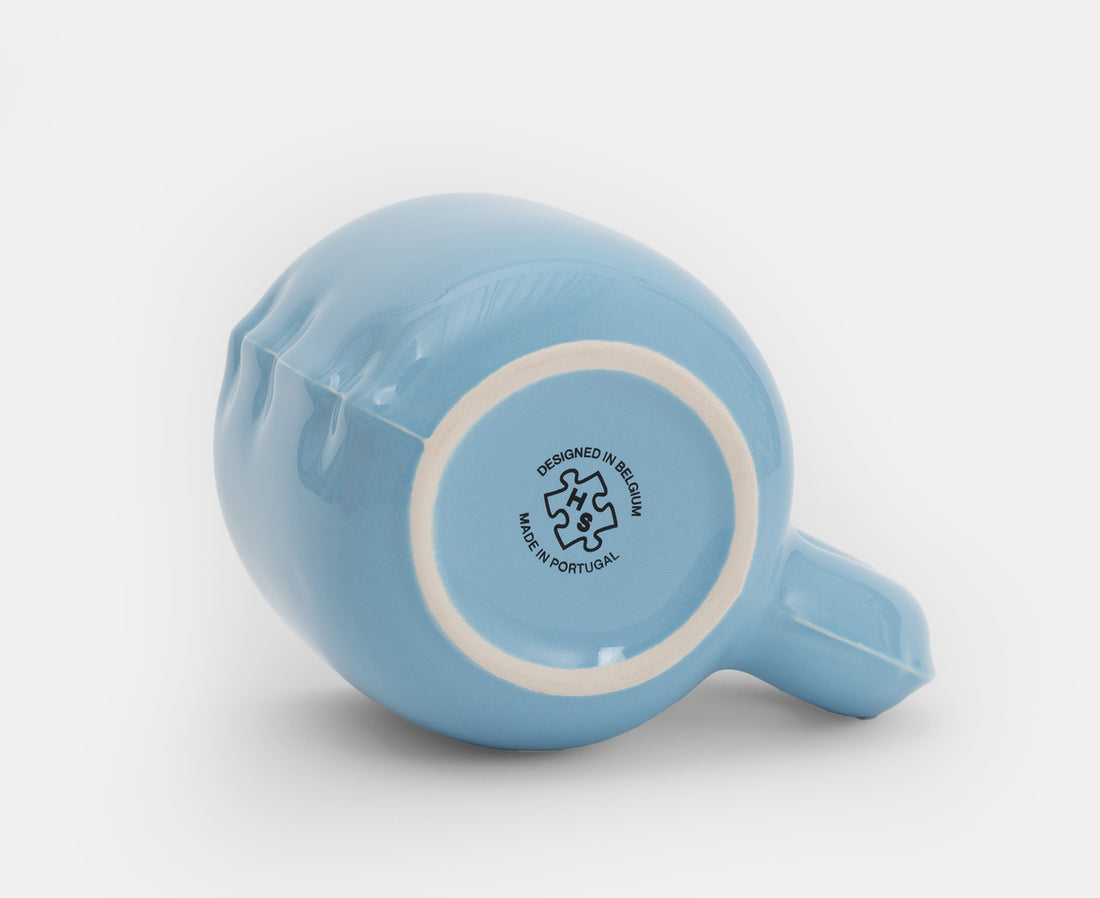 The bottom of a light blue ceramic Gaston Blow Up Mug by Home Studyo with a sculpted, organic handle and side details.