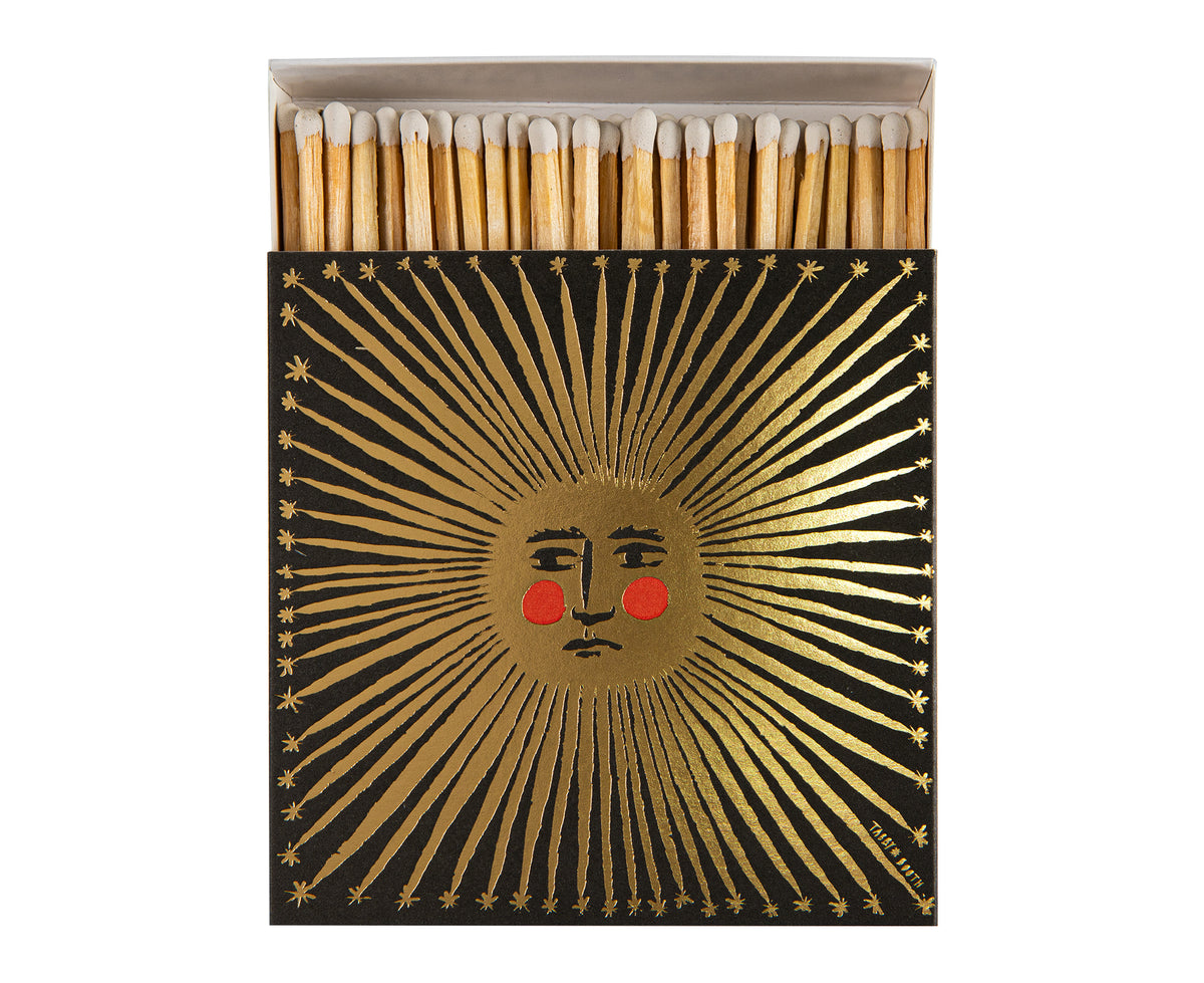 A matchbox with a black cover featuring a metallic gold sun design and red cheeks.