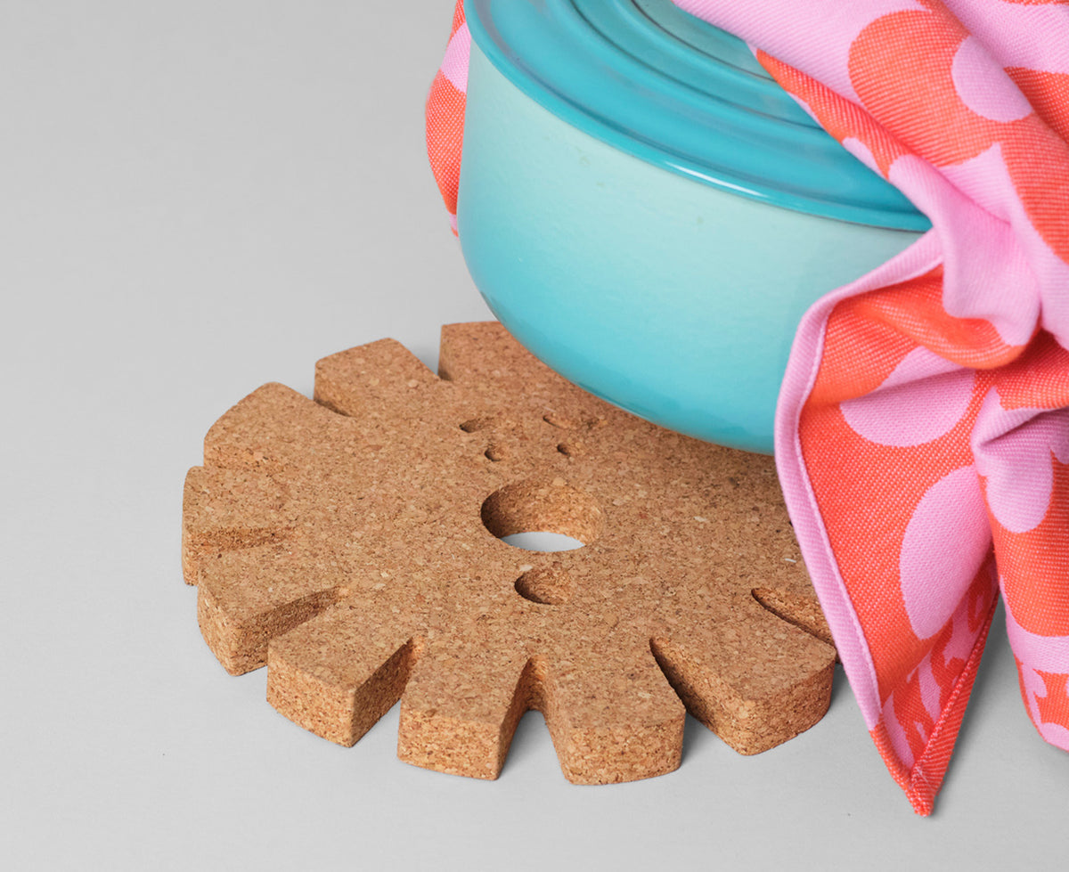 Sun Face Medium Cork Trivet by Wrap on a able with a casserole pot.
