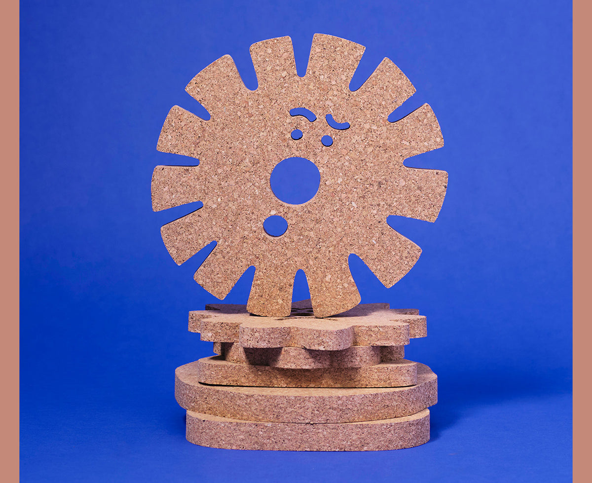 Sun Face Medium Cork Trivet by Wrap on a stack of trivets on a bright blue background.