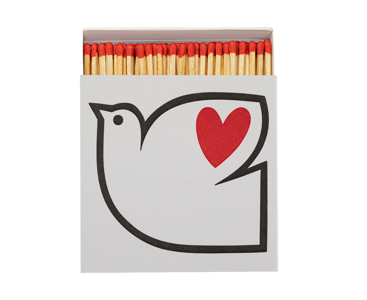 A matchbox with a white cover featuring a black dove outline and a red heart, with red-tipped wooden matches visible inside.