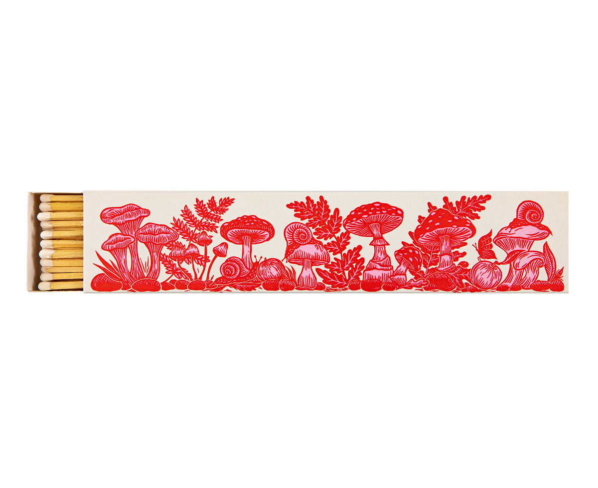 A matchbox containing light wood matches, decorated with a red illustrated border of mushrooms, ferns, and foliage on a white background.