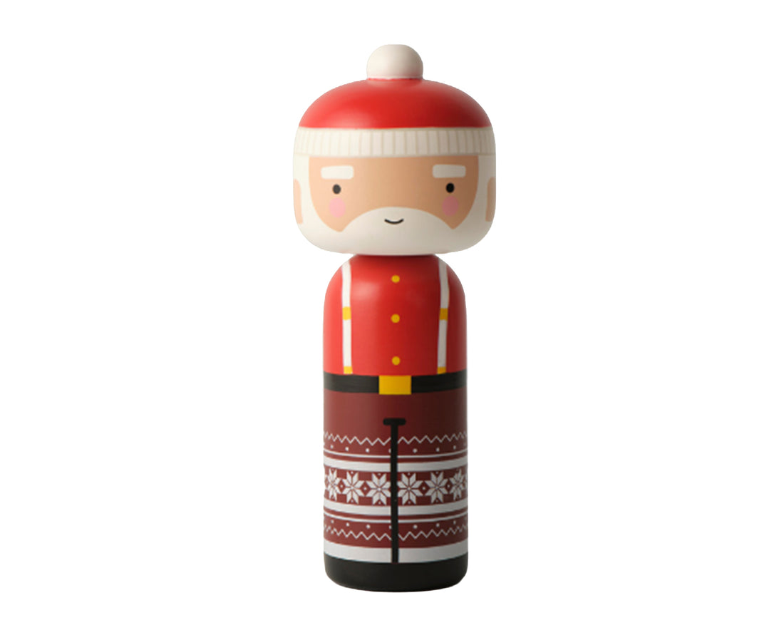 A Santa Claus-themed wooden kokeshi doll with a red hat, white beard, red jacket with yellow buttons, and a brown patterned skirt with white snowflakes, isolated on a white background.
