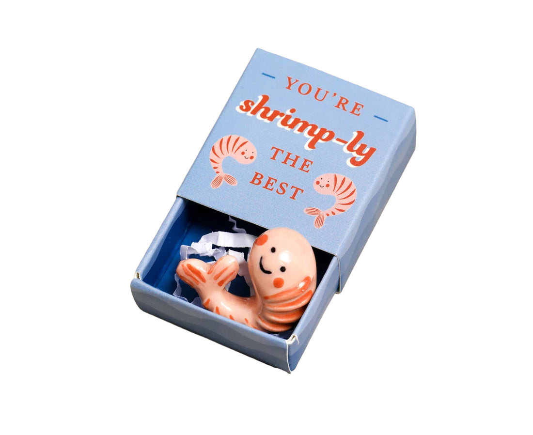 A small novelty gift set in a light blue matchbox-style box with the lid partially open. The box lid reads &