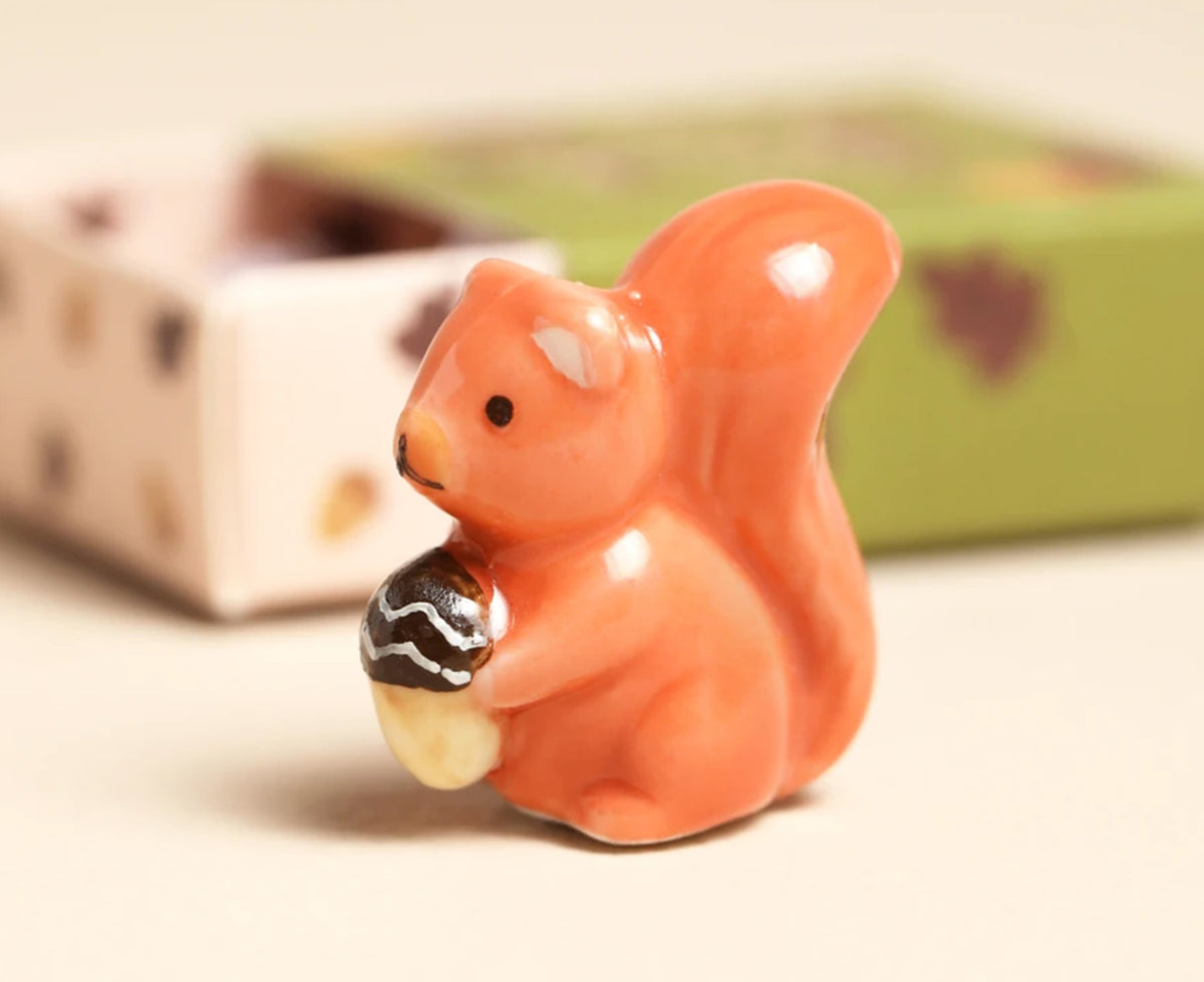 ceramic orange squirrel figurine holding an acorn next to a small box.