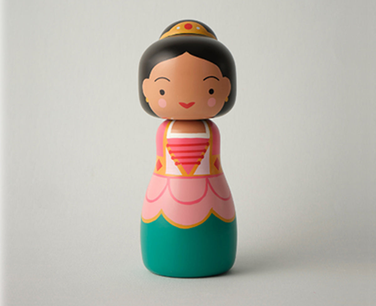 A stylized wooden Sugarplum Fairy kokeshi doll with a round head, black hair, a gold crown, and a pink and teal dress, shown on a plain gray background.