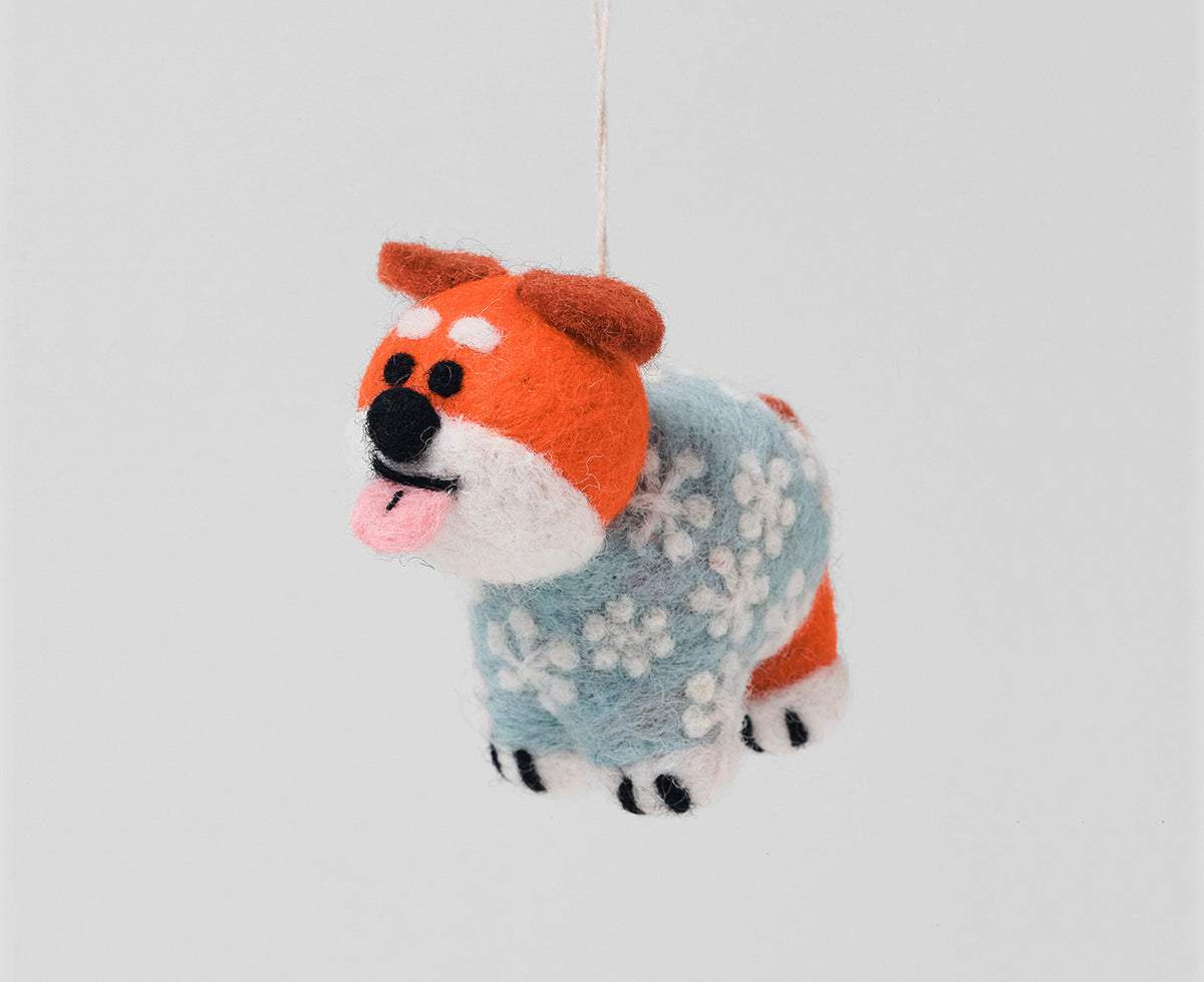 A handcrafted felt dog ornament wearing a light blue and white patterned sweater, hanging against a solid light gray background.